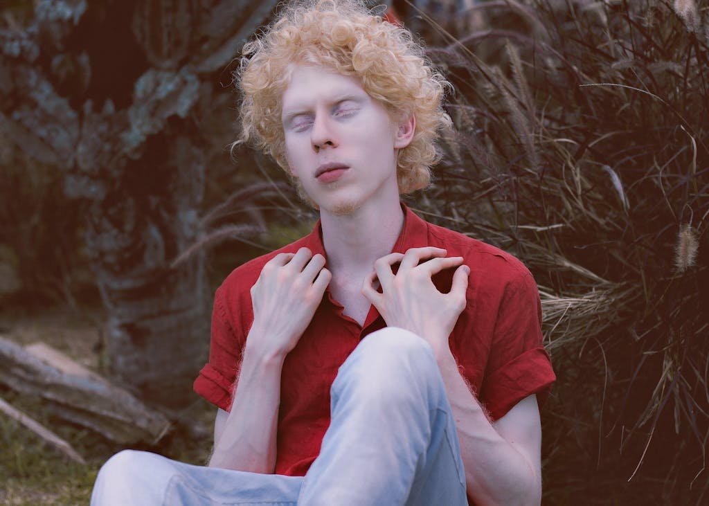 A young man with closed eyes meditates serenely in an outdoor setting, surrounded by natural scenery.
