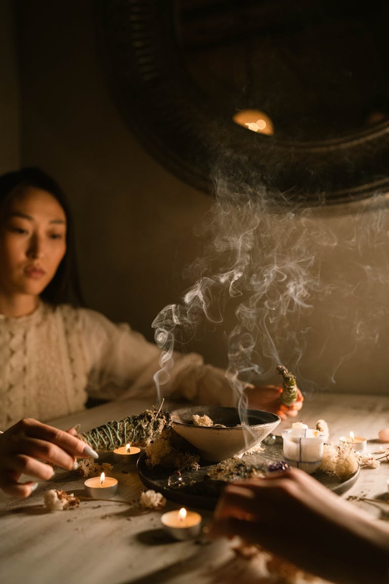 Asian woman engaging in a mystical ritual with candles and herbs indoors.